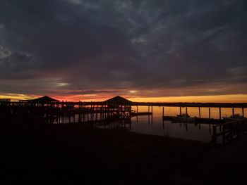 Silhouette pier on beach against dramatic sky during sunset