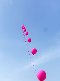 Low angle view of pink balloons flying against blue sky