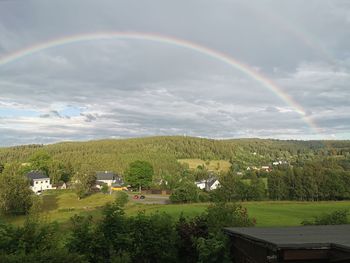 Scenic view of rainbow over trees and houses against sky