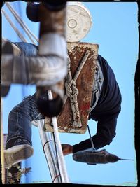 Low angle view of man working on rope against sky