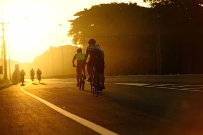 Men riding bicycles on road during sunset