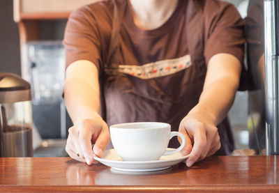 Midsection of woman holding coffee at table