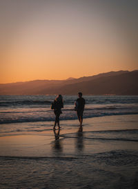 Silhouette people on beach against sky during sunset