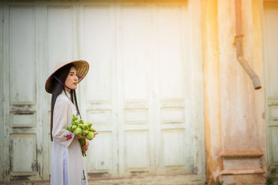 Side view of young woman holding buds against building