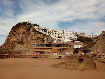 Woman sitting on rock against buildings at azenhas do mar