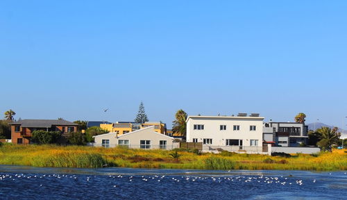 Houses by river and buildings against clear blue sky
