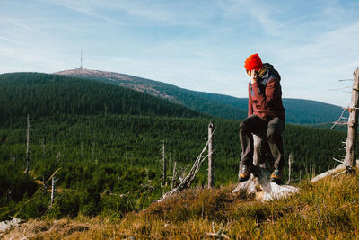 Woman sitting on tree stump against sky