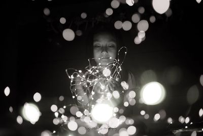 Close-up of girl holding illuminated christmas lights at night