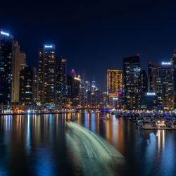 Illuminated buildings by river against sky at night