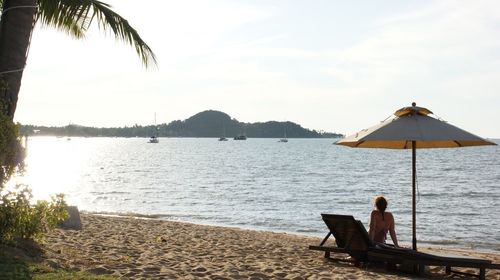 Woman sitting on beach against sky