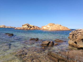 Scenic view of rocks in sea against clear blue sky