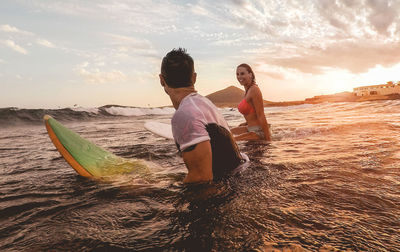 Couple standing with surfboard in sea against sky