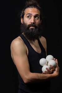 Bearded man with balls standing against black background