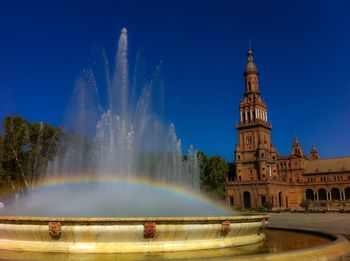 Rainbow on fountain at plaza de espana against clear blue sky