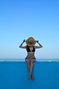 Woman covering face with hat while sitting at beach