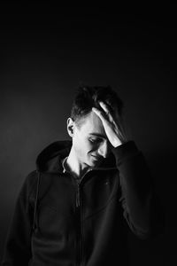 Young man with hand in hair against black background