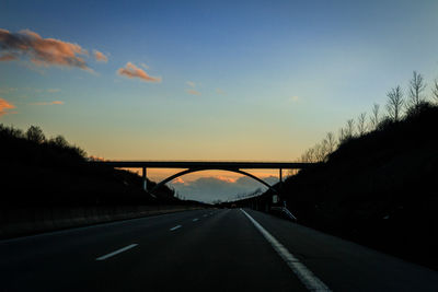 Bridge over highway against sky during sunset
