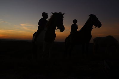 Silhouette people riding on field  sky during sunset