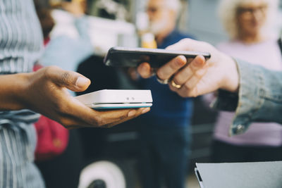 Cropped hand of customer paying through smart phone in city