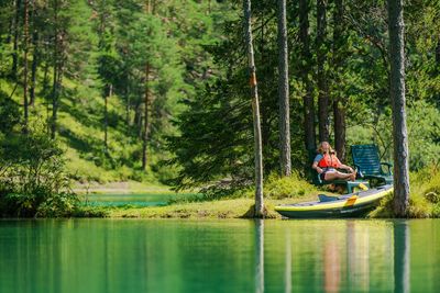 Woman resting on chair on lakeshore in forest