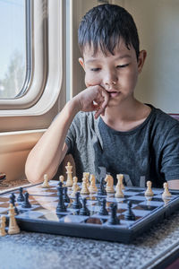 Asian boy pondering a move in a game of chess sitting in the train