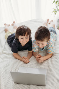 Children use technology. online learning at home. the boys lie on the bed and look at the laptop. 