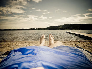 Low section of person relaxing on lake against sky