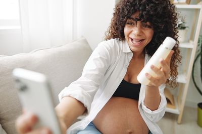 Young woman using mobile phone while sitting on bed at home