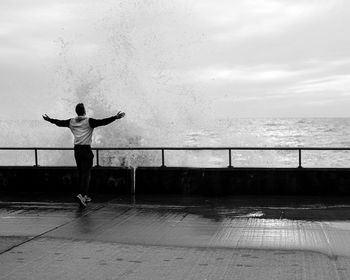 Man with arms outstretched standing by water splash at promenade