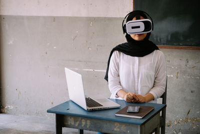 Teacher wearing virtual reality simulator while sitting in classroom