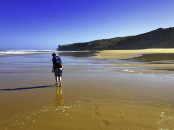 Rear view of woman walking on beach against clear sky