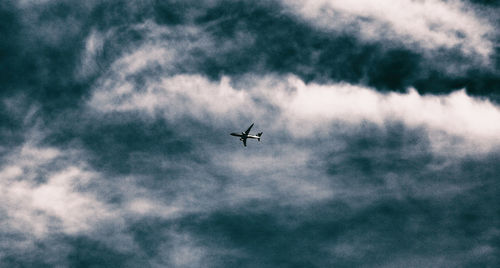 Low angle view of airplane flying in cloudy sky