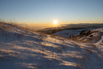 Snow covered field against sky during sunset