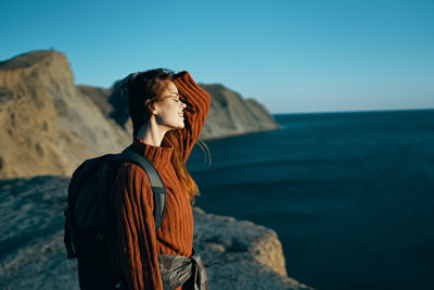 Man standing on rock looking at sea shore against sky