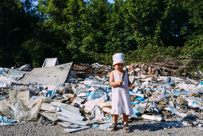 Little girl at a dump among a heap of scattered garbage in the forest.