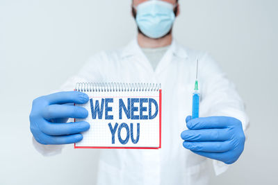 Midsection of doctor wearing mask holding syringe against white background