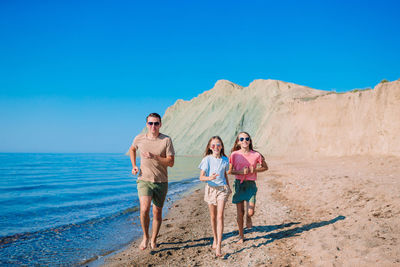 Full length of father and daughter on shore against sky