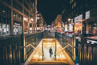 People on illuminated street amidst buildings at night