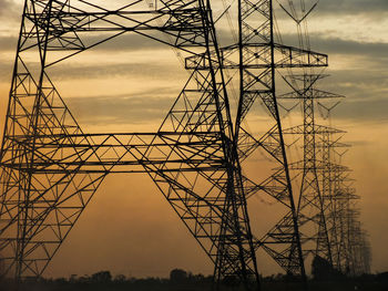 Low angle view of silhouette electricity pylon against sky during sunset