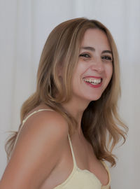Close-up portrait of happy young woman wearing bra by white curtain