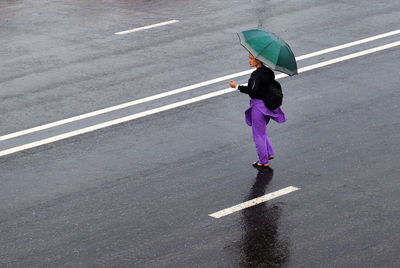 Full length of woman with umbrella on road in rain