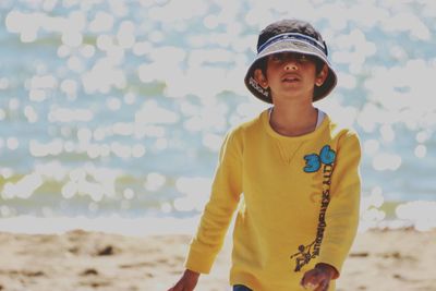 Portrait of boy wearing hat walking on beach during sunny day