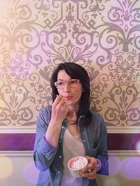 Portrait of mid adult woman eating ice cream against patterned wall at home