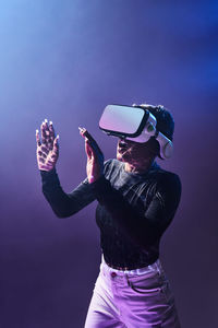 Astonished female african american gamer in modern vr goggles standing on dark background in studio while experiencing virtual reality in neon illumination