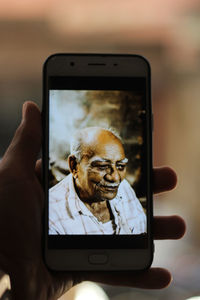 Cropped hand holding mobile phone with photograph of senior man