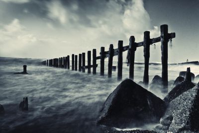 Wooden posts in sea against sky