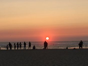 Silhouette people on beach against sky during sunset