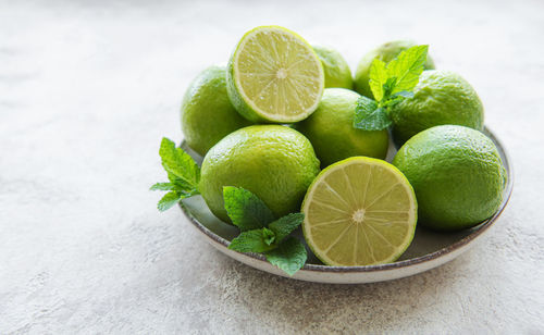 Green limes with fresh mint leaves on plate, concrete background