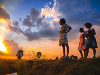 Rear view of woman standing on field against sky during sunset