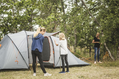 Siblings preparing tent in forest at camping site